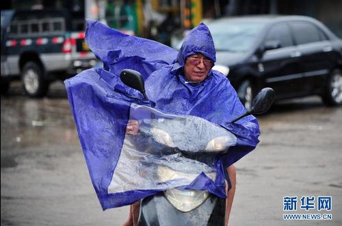 7月18日，在文昌街头，路人在暴风雨中骑行。新华社记者 郭程